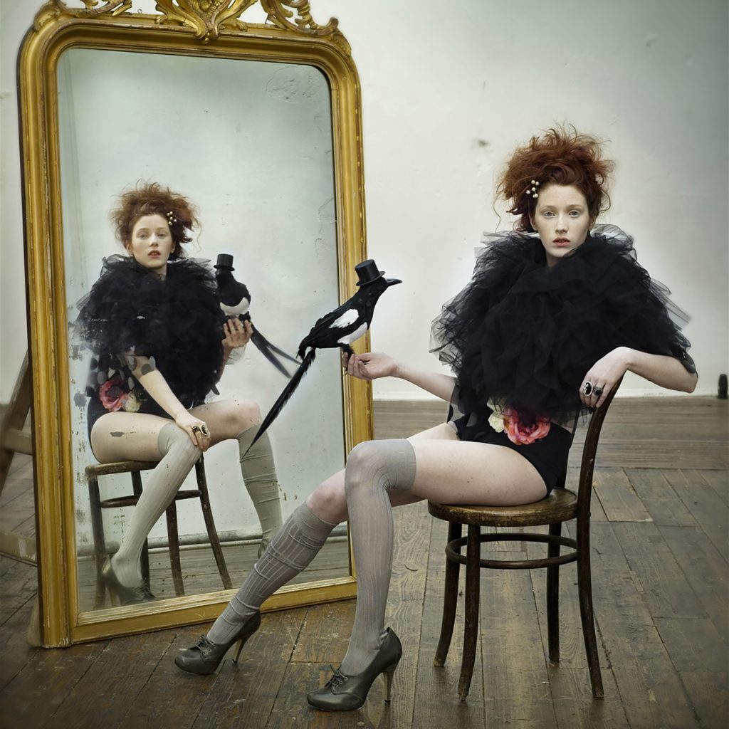 fashion editorial studio shoot of a redhead female , model in front of the mirror with vintage props wearing contemporary irish design